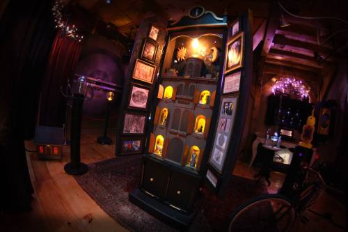 A dimly lit room featuring a decorative cabinet with glowing shelves, surrounded by vintage decor and mysterious artifacts.
