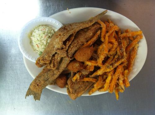 A plate of fried fish, hushpuppies, and sweet potato fries, accompanied by a side of coleslaw.