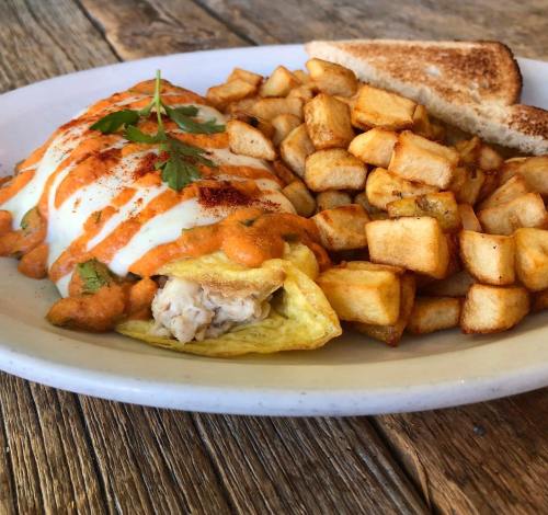 A plate featuring an omelette topped with sauce, served with crispy potatoes and toast, garnished with cilantro.