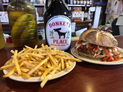 A plate of golden fries next to a poppy seed bun sandwich with toppings, alongside a large bottle of Donkey's Place.