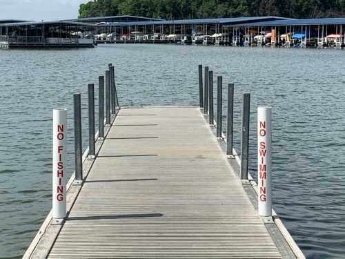 A wooden dock extends over calm water, with signs stating "No Fishing" and "No Swimming" on either side.