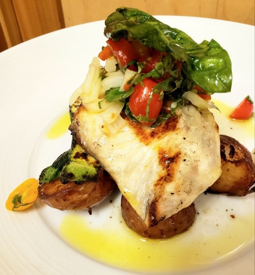 Grilled fish fillet topped with fresh salsa, served on roasted potatoes and garnished with greens.
