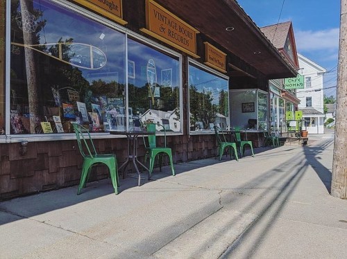 A quaint street scene featuring a vintage bookstore with green chairs outside and a clear blue sky.