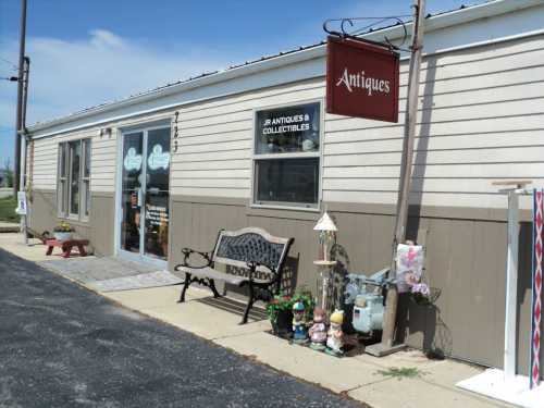 A quaint antique shop with a sign, bench, and decorative items outside, set against a clear blue sky.