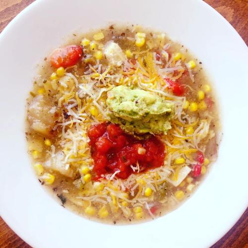 A bowl of soup with corn, tomatoes, cheese, guacamole, and salsa, garnished with herbs.