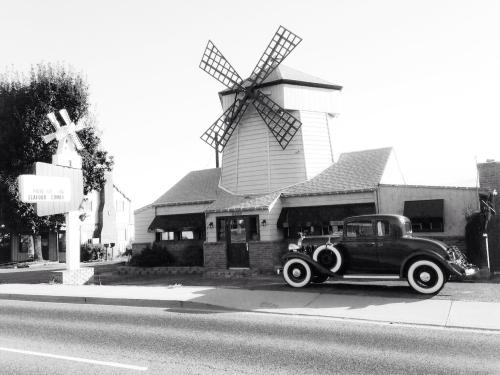 A vintage car parked in front of a windmill-shaped building, with a sign for a seafood restaurant nearby.