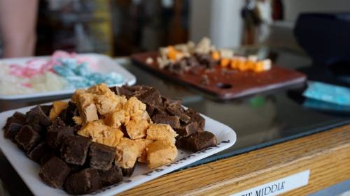 A plate of assorted fudge pieces in various flavors, with more fudge displayed in the background.