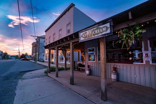 A charming ice cream shop at dusk, with colorful skies and warm lights illuminating the entrance.
