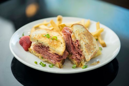 A plate with a sliced sandwich filled with layers of meat, served with fries and a strawberry on the side.