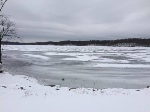 A frozen lake surrounded by snow-covered land under a cloudy sky.