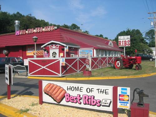 A red and white barbecue restaurant with a sign reading "Home of the Best Ribs" and a vintage tractor in front.