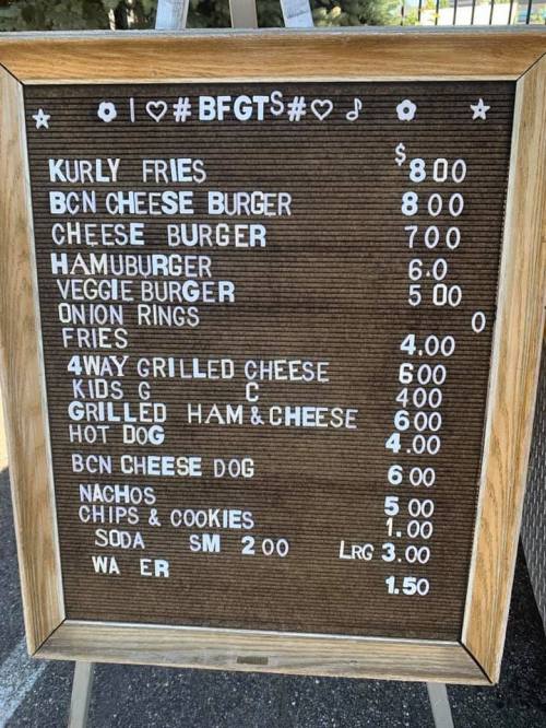 Menu board displaying food items and prices, including burgers, fries, nachos, and drinks.
