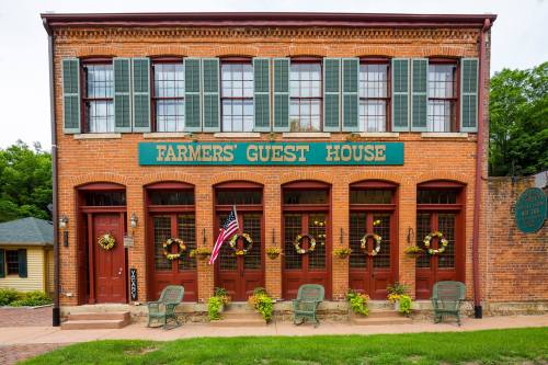 Historic brick building with green shutters, sign reading "Farmers' Guest House," and decorated with wreaths and planters.