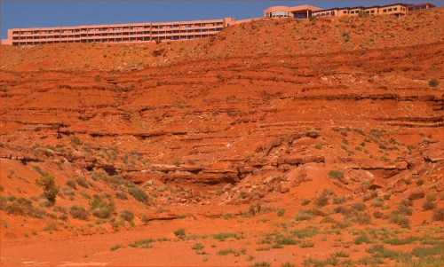 A multi-story building sits atop a red rock cliff, surrounded by arid terrain and sparse vegetation.