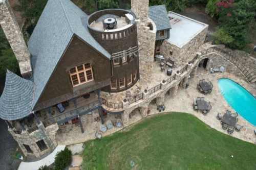 Aerial view of a stone mansion with a pool, surrounded by greenery and outdoor seating areas.