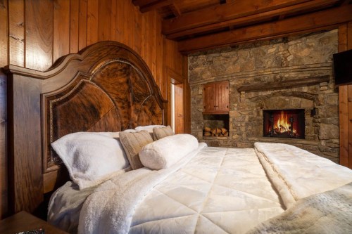 Cozy bedroom with a wooden bed, plush bedding, and a stone fireplace, creating a warm, inviting atmosphere.