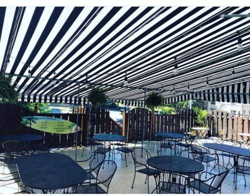 Outdoor dining area with black and white striped awning, featuring metal tables and hanging plants.