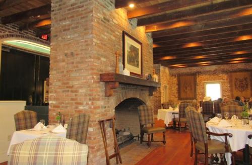 Cozy restaurant interior featuring brick walls, wooden beams, a fireplace, and elegantly set tables.