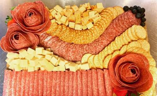 A colorful charcuterie board featuring meats, cheeses, crackers, and decorative rose-shaped salami.