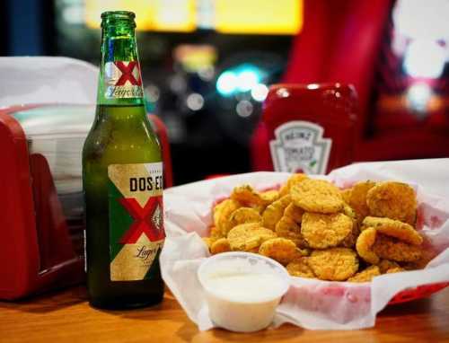 A plate of golden fried chicken nuggets with a side of ranch dressing, a bottle of Dos Equis beer, and ketchup.