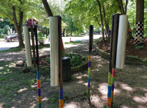A group of tall, metallic tubes on colorful poles in a park, surrounded by trees and a pathway.
