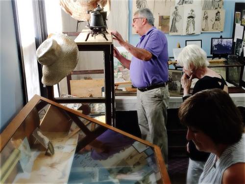 A man and two women examine exhibits in a museum, with artifacts and displays visible in the background.