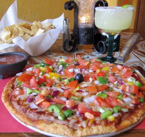 A colorful veggie pizza topped with tomatoes, peppers, and onions, served with chips, salsa, and a margarita.