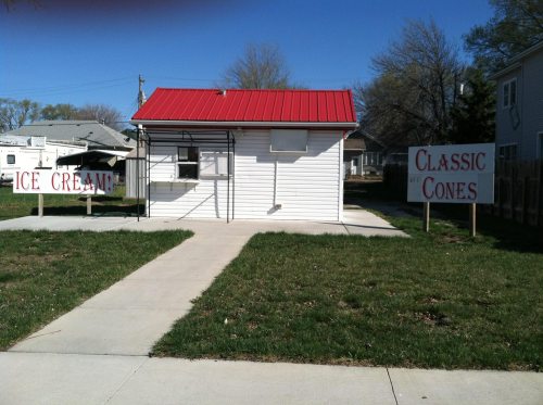 A small ice cream stand with a red roof, surrounded by grass and signs for "Ice Cream" and "Classic Cones."