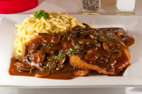 A plate of breaded meat topped with mushroom gravy, served with creamy pasta and garnished with parsley.