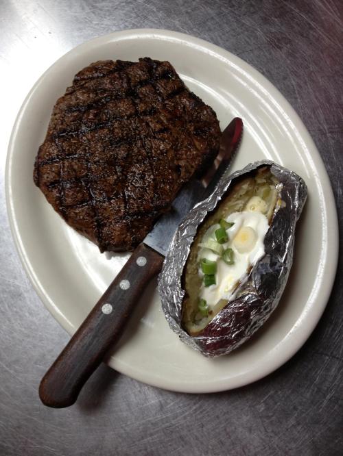 A grilled steak with grill marks next to a baked potato topped with sour cream and green onions, served on a plate.