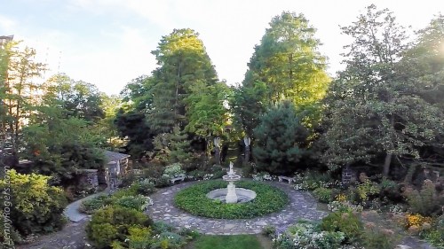 A serene garden with a central fountain, surrounded by lush trees and colorful flowers, creating a peaceful atmosphere.
