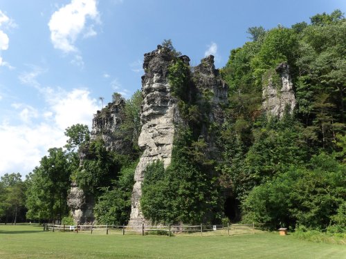 A tall rock formation surrounded by lush greenery under a clear blue sky.