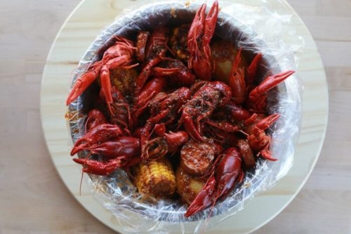 A bowl filled with spicy crawfish, corn, and sausage, all mixed together and ready to eat.