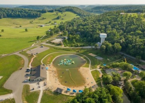 Aerial view of a recreational area with a pond, inflatable water toys, and green hills in the background.