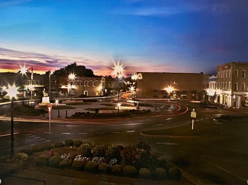 A twilight scene of a town square with streetlights, a roundabout, and buildings, creating a serene atmosphere.