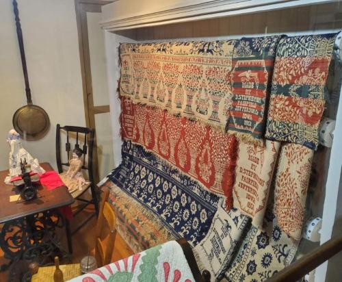 A display of colorful textiles and tapestries hanging on a wall, with a wooden chair and table in the foreground.