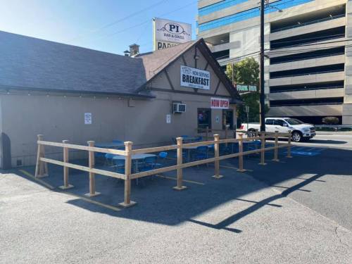 A small restaurant with a wooden fence and outdoor seating, featuring a sign that says "Now Open" and "Breakfast."