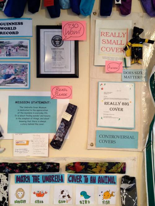 A wall display featuring a Guinness World Record certificate, mission statement, and various colorful umbrella covers.