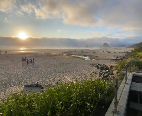 A serene beach at sunset, with people walking along the shore and rocky formations in the distance under a cloudy sky.