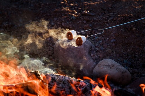 Two marshmallows roasting over a campfire, with smoke rising and glowing embers in the foreground.