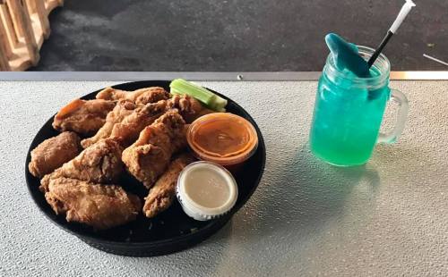 A plate of crispy fried chicken wings with dipping sauces and a blue drink in a mason jar on a table.