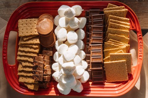 A red tray filled with graham crackers, chocolate bars, marshmallows, and peanut butter cups, arranged neatly.
