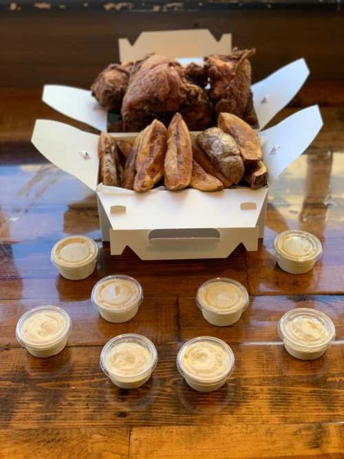 A takeout box filled with fried chicken and sweet potato fries, surrounded by small containers of dipping sauce.