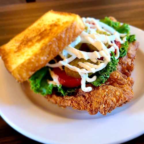 A crispy fried chicken sandwich with lettuce, tomato, pickles, and mayonnaise, served on toasted bread.