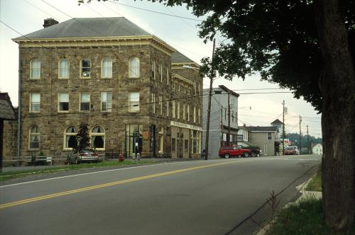 Historic stone building on a quiet street, with parked cars and trees lining the road.
