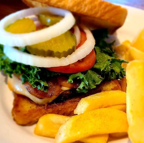 A close-up of a burger with lettuce, tomato, pickles, and onion, served with golden fries on the side.