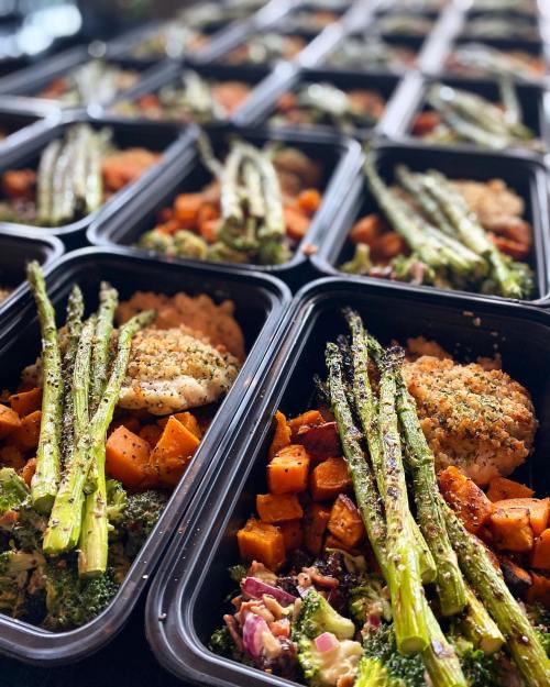 Meal prep containers filled with seasoned chicken, roasted sweet potatoes, and asparagus, arranged neatly in rows.