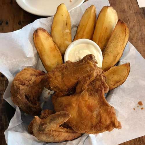 A plate with crispy fried chicken, golden potato wedges, and a small bowl of dipping sauce.