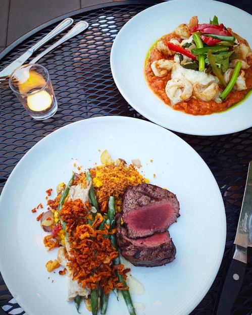 A plate featuring a steak with green beans and crispy onions, alongside a shrimp dish with vegetables in sauce.