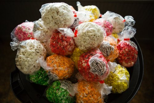 A colorful assortment of popcorn balls in clear bags, stacked on a black surface.